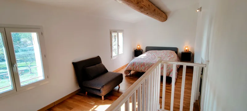 Vue d’ensemble de la chambre à l’étage, avec lit double, fauteuil et garde-corps blanc