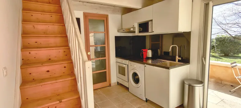 Cuisine aux meubles blancs et crédence sombre, à côté de l’escalier en bois