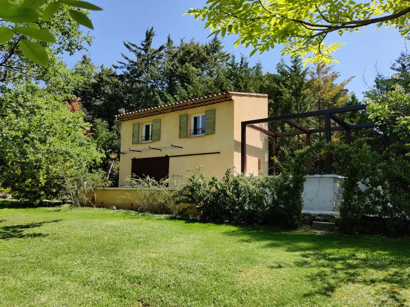Façade du cottage entourée de feuillage avec pergola sur le côté