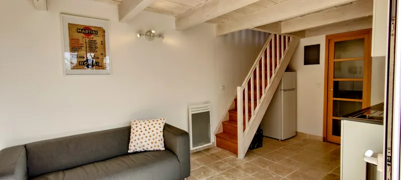 Canapé gris sous l’escalier blanc et bois qui mène à la chambre