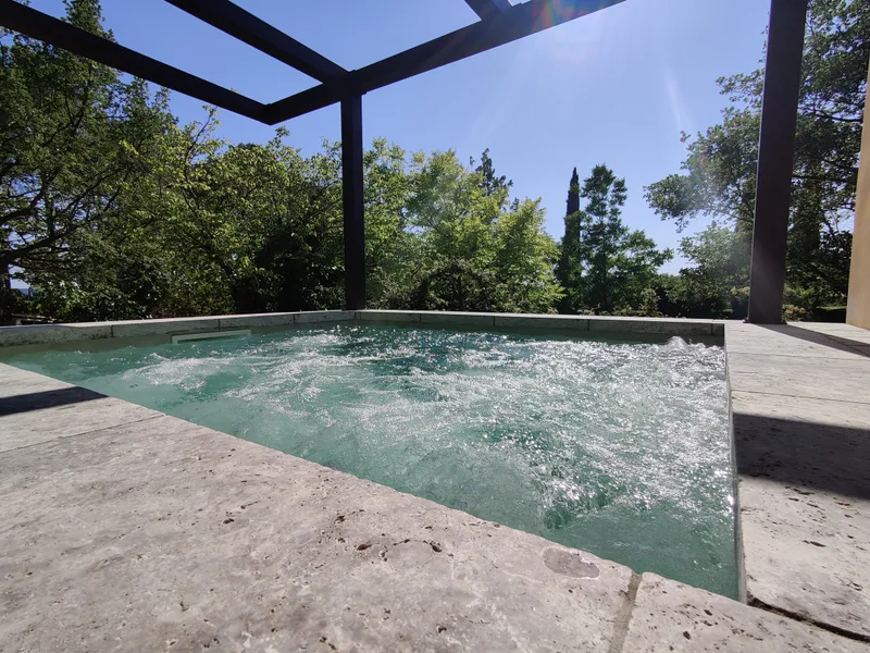 Margelle en pierre au premier plan et piscine SPA en mouvement sous la pergola