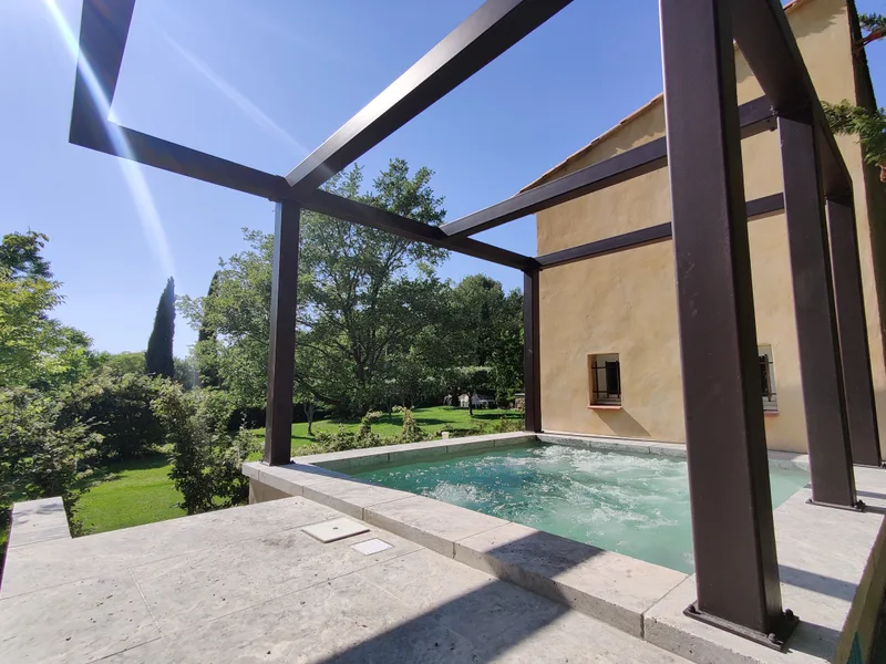 Vue d’ensemble de la piscine SPA sous sa pergola, à côté de la façade jaune du Mazet