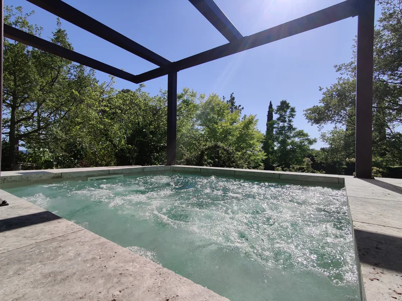 Eau bouillonnante de la piscine SPA sous la pergola, entourée d’arbres