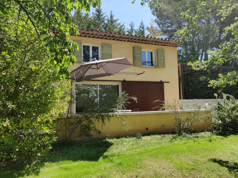 Façade jaune et terrasse du Mazet avec pergola, entourées de végétation